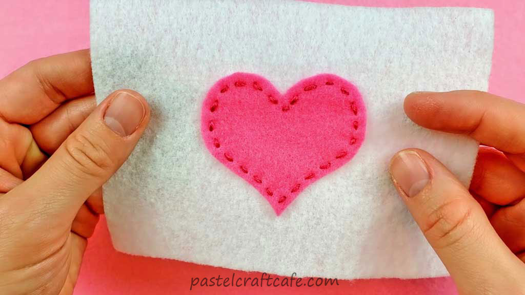A finished look of the pink heart applique attached to the white felt using the running stitch