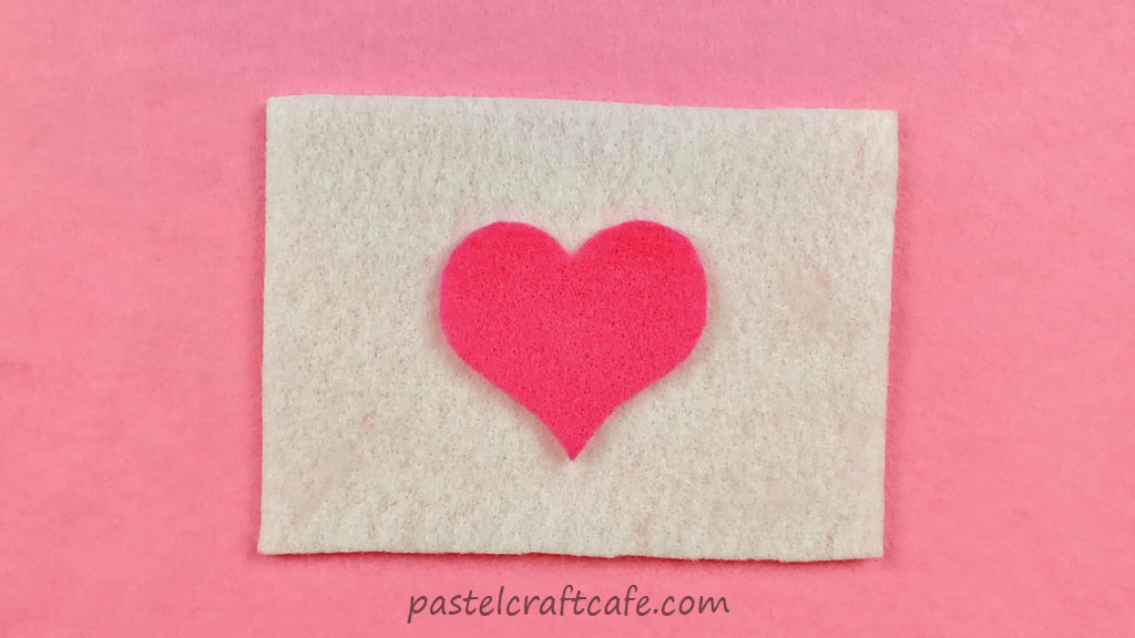 A piece of white felt with a pink felt heart on top