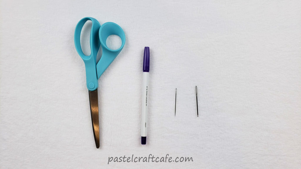Scissors, fabric marking pen, embroidery needle, and a yarn needle