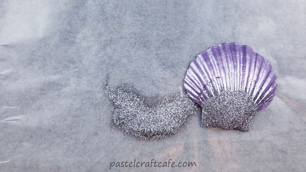 A purple seashell with silver glitter next to a pile of more silver glitter