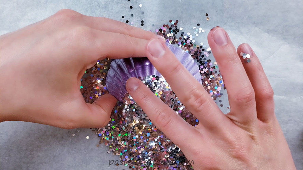 Tapping chunky holographic glitter onto a purple seashell