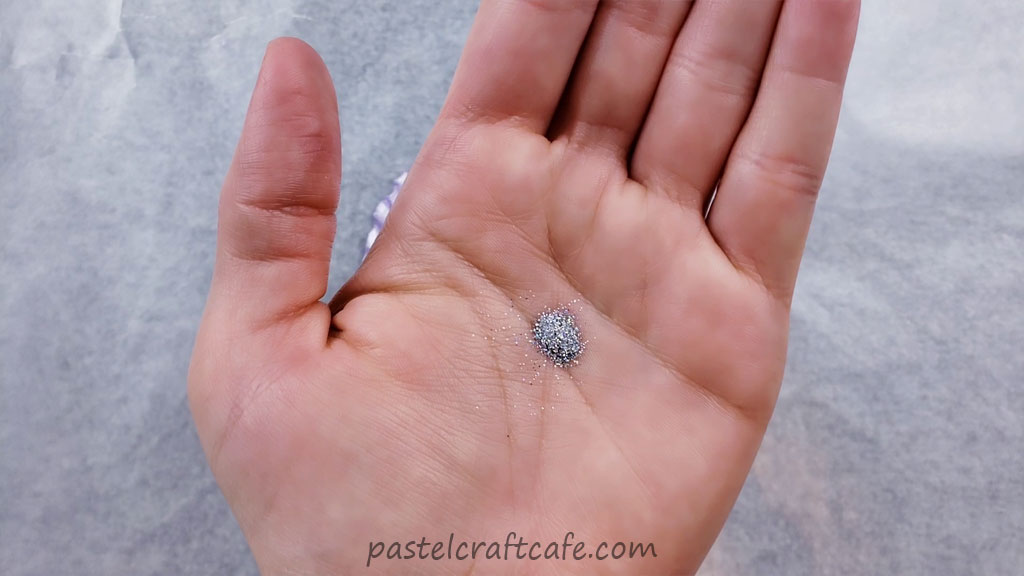 A hand with a pinch of fine silver holographic glitter