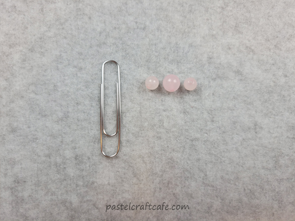 A paperclip and three rose quartz beads of varying sizes
