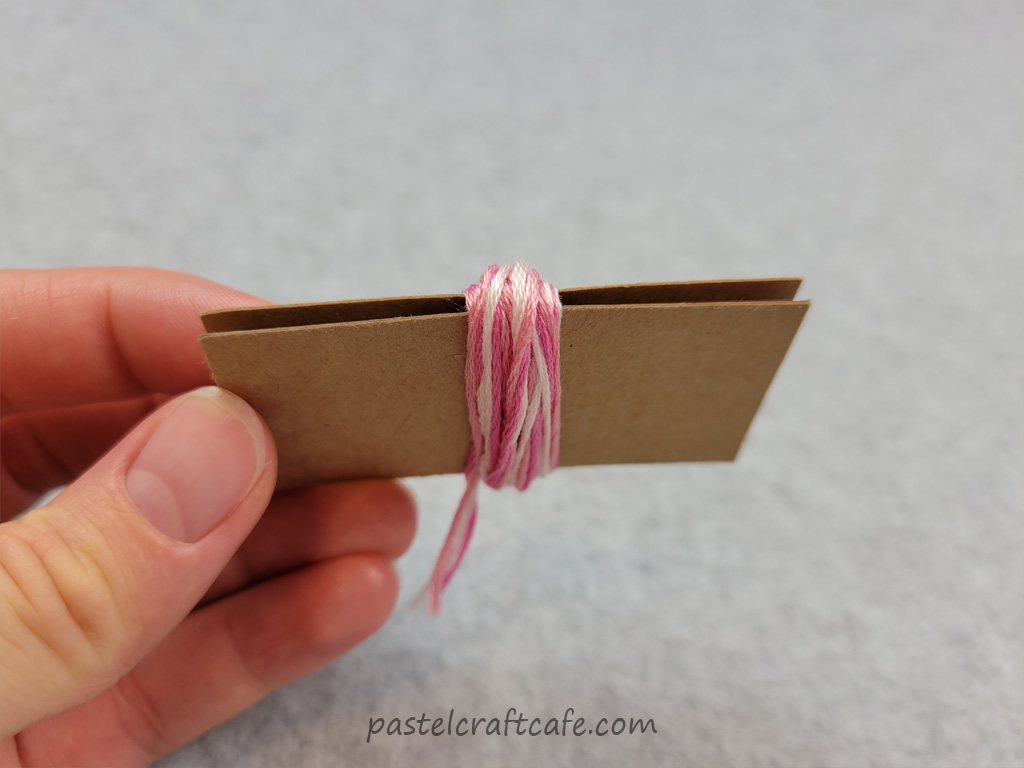 The top view of a bundle of multicolored embroidery floss wound around a DIY mini tassel maker with tails of floss cut