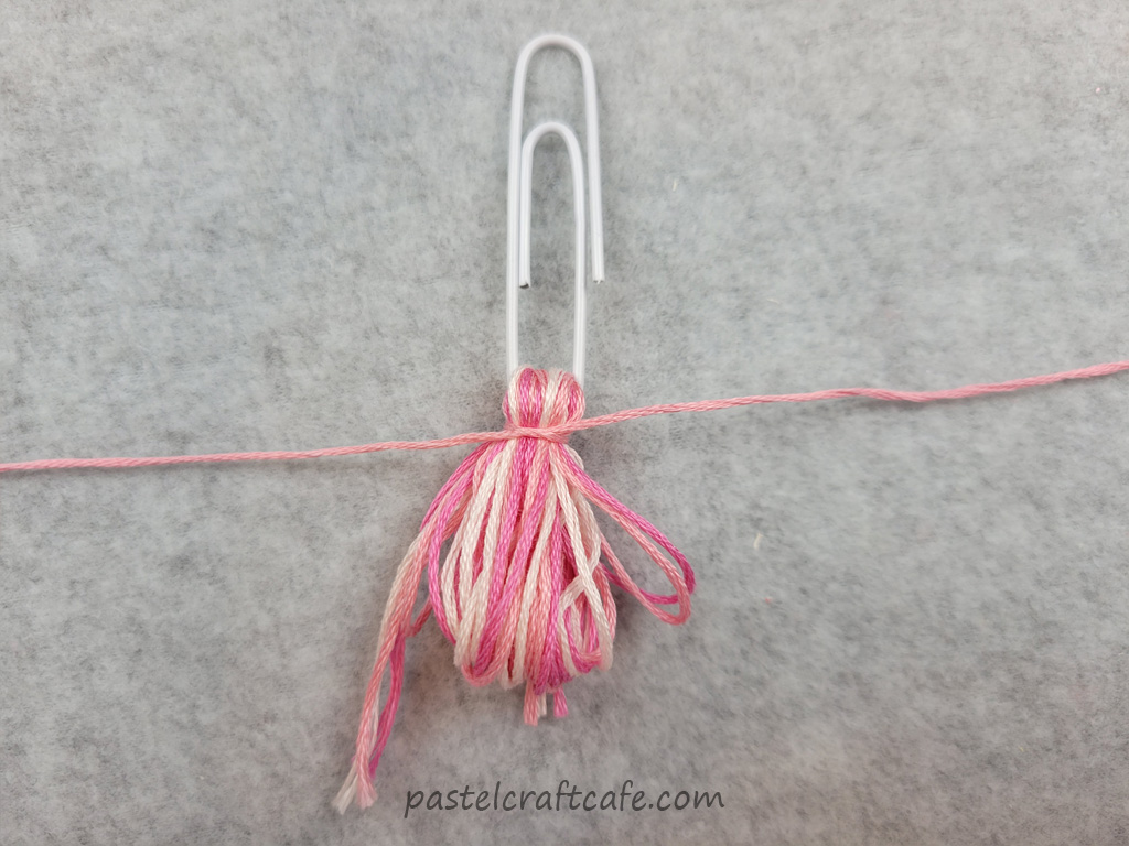 A piece of embroidery floss being tied onto the top of a bundle of embroidery floss