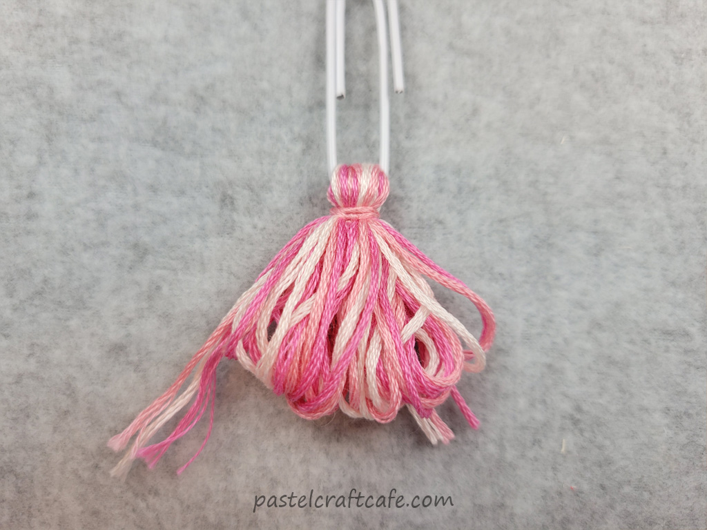 An unfinished tassel with loops attached to a paperclip