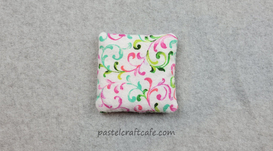 A finished microwavable hand warmer with a pink, green, and teal scroll pattern on a white background