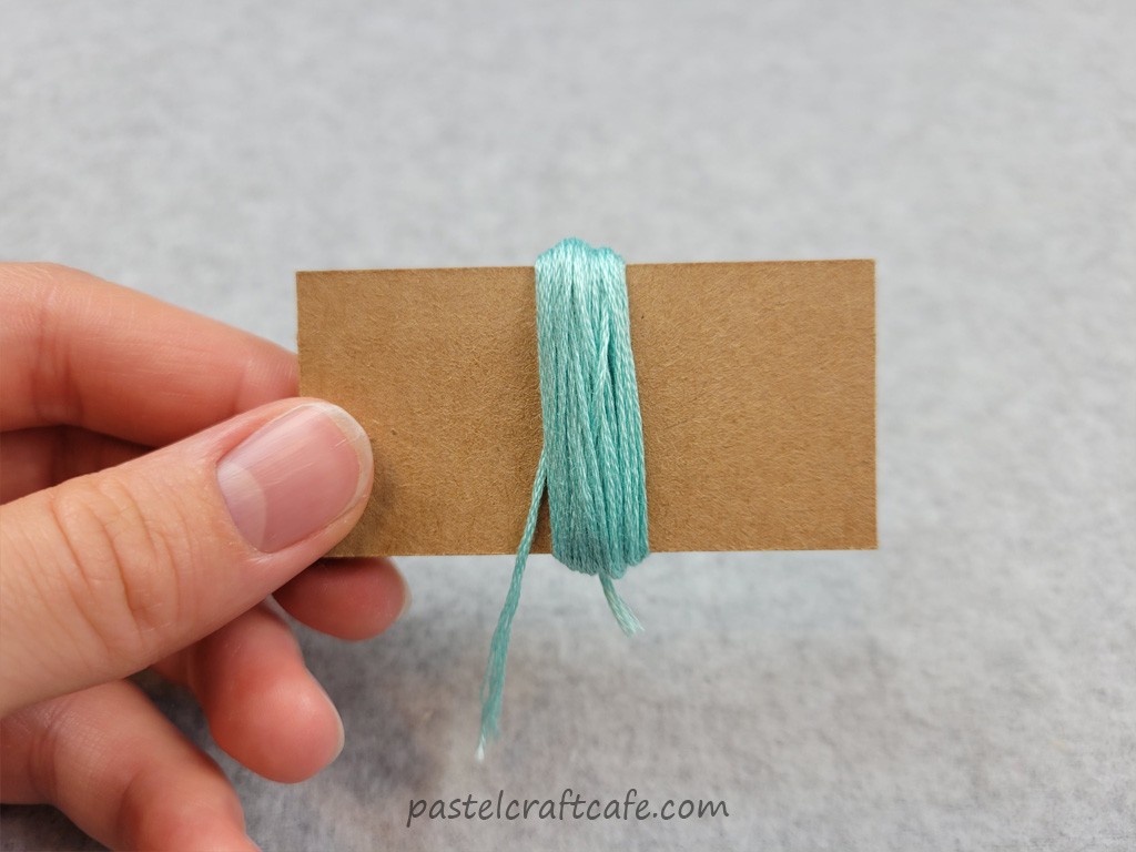 Embroidery floss fully wrapped around a DIY mini tassel maker with end of floss cut