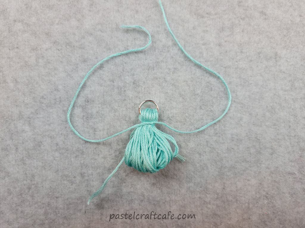 A bundle of embroidery floss with a jump ring at the top and a string tied around the top of the bundle