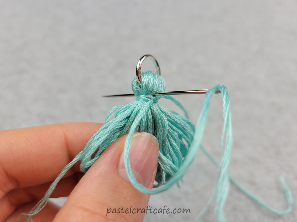 Needle threaded with embroidery floss poking through top of tassel