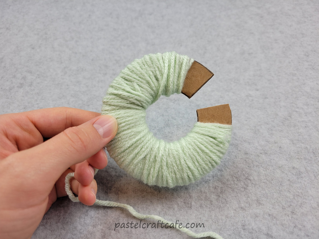 A pom pom circle template with green yarn wound around the circle