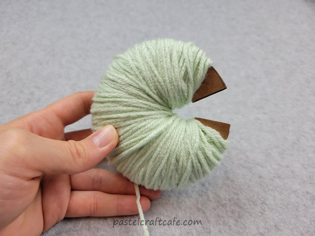 A pom pom circle template completely full with green yarn
