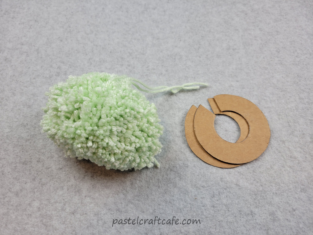 An unfinished circle template pom pom next to the circle template pieces