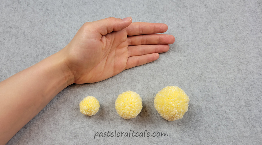a hand above three pom poms of different sizes