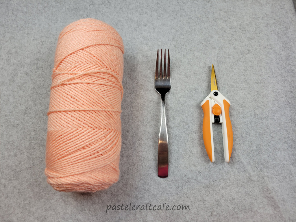 A skein of peach yarn, a fork, and scissors