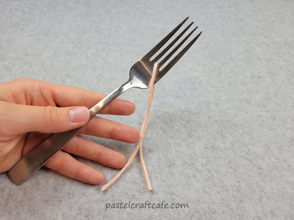 A piece of yarn in between the tines of a fork