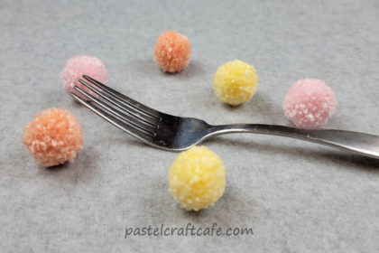 a metal fork surrounded by small pom poms in pink, orange, and yellow