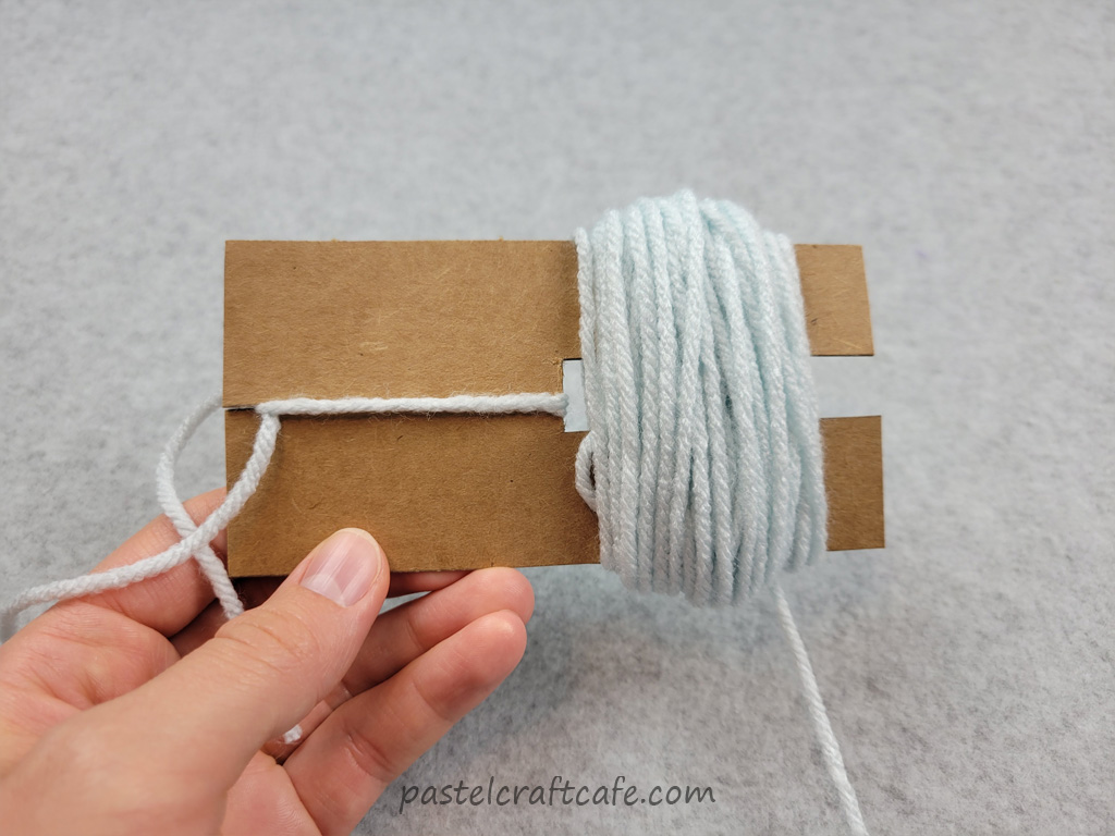 A pom pom rectangle template with some yarn wound around the outside
