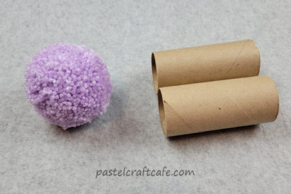 a large purple pom pom next to two empty toilet paper tubes
