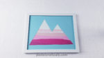 a frame with a silhouette of a mountain with two peaks made with ripped strips of pink and white paper on a blue background