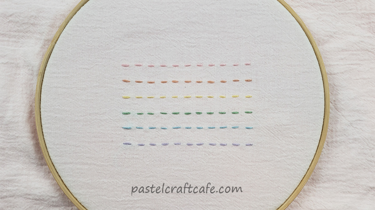 an embroidery hoop with six horizontal lines of the running stitch, each a different color: pink, orange, yellow, green, light blue, and lavender