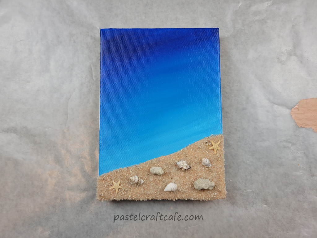 A mixed media beach canvas after a layer of Mod Podge which has dried