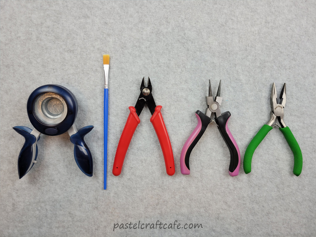 A circle paper puncher, a paintbrush, wire cutters, round nose pliers and chain nose pliers