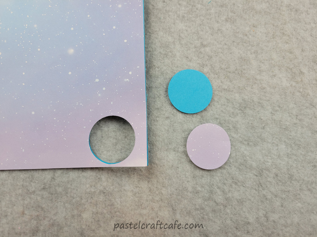 A piece of scrapbook paper and cardstock with a circle punched out of it with the circles of punched paper sitting beside it