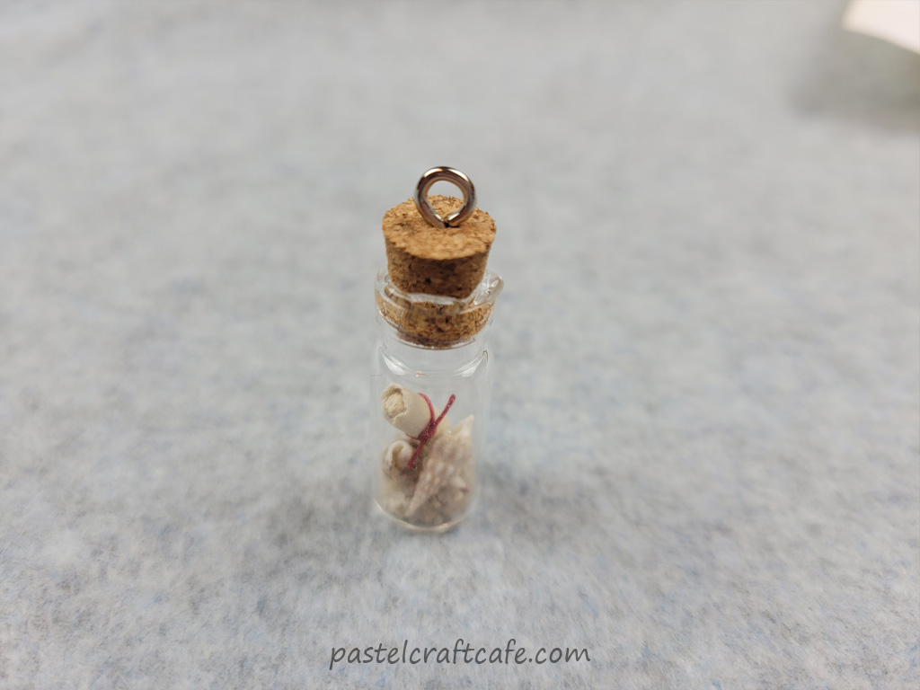 A cork added to a message in a bottle necklace charm with glue oozing over the bottle