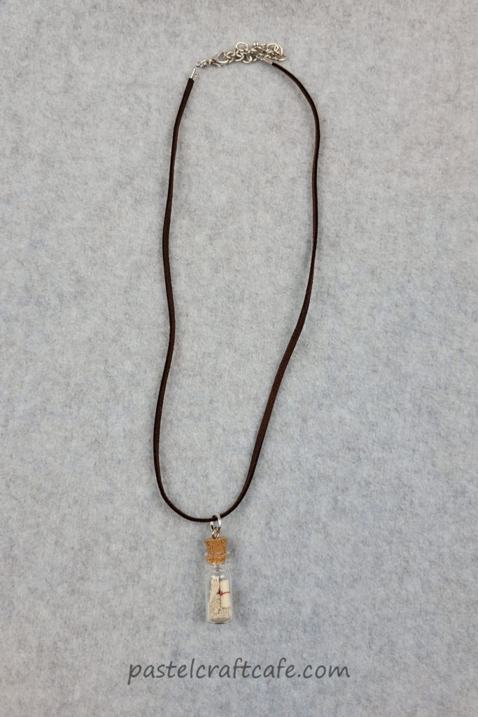 A finished message in a bottle necklace laid out lengthwise