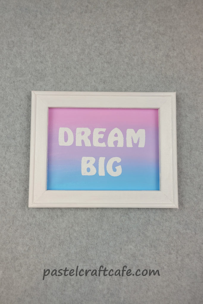A reverse canvas with a white frame and a gradient pastel background with the words "DREAM BIG" stenciled in white