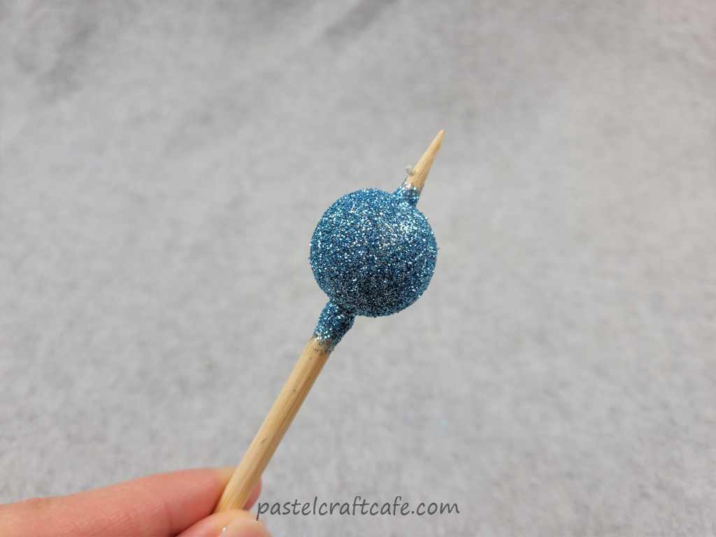 A wooden bead after two layers of blue glitter to get even coverage