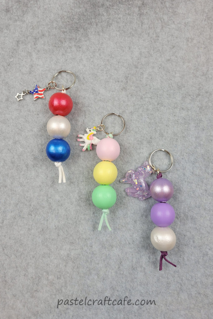 Three finished wood bead keychains with various painted beads and charms in different styles