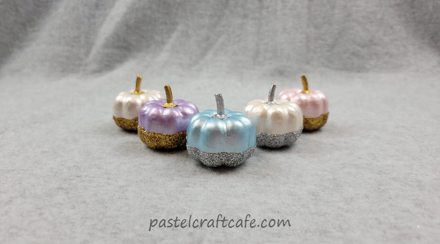 Five painted and glitter dipped pumpkins arranged in a V formation