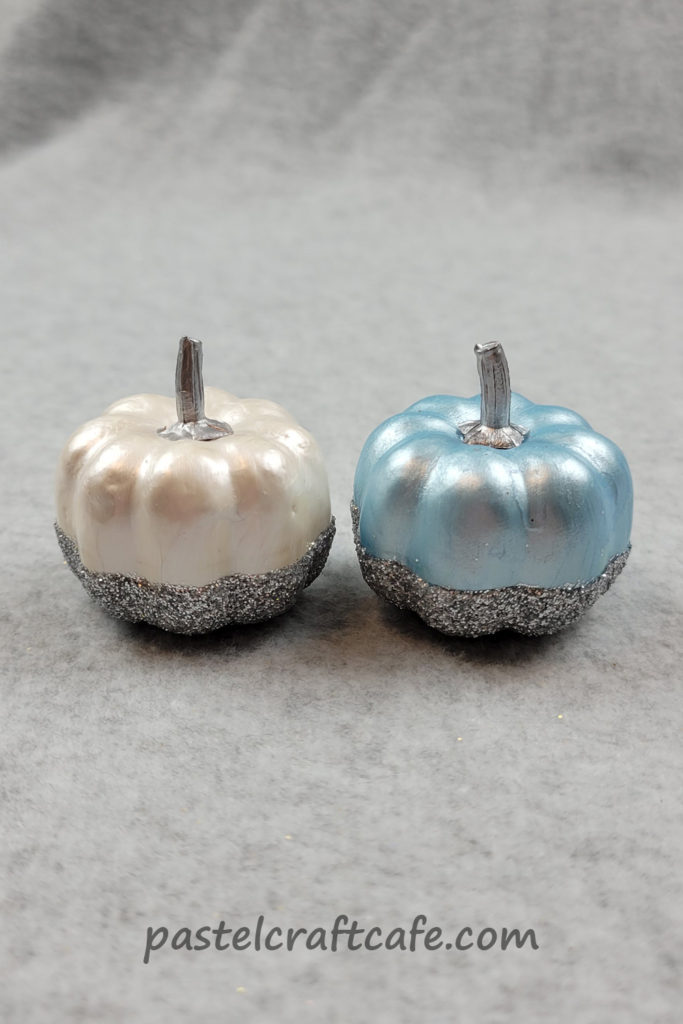 A white painted pumpkin and blue painted pumpkin both with silver glitter