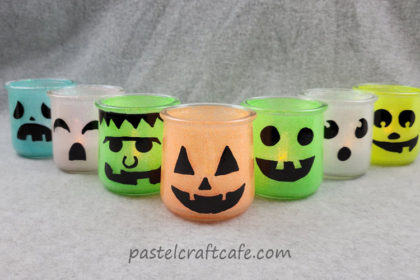 Seven glitter halloween luminary jars with various character faces in a V formation