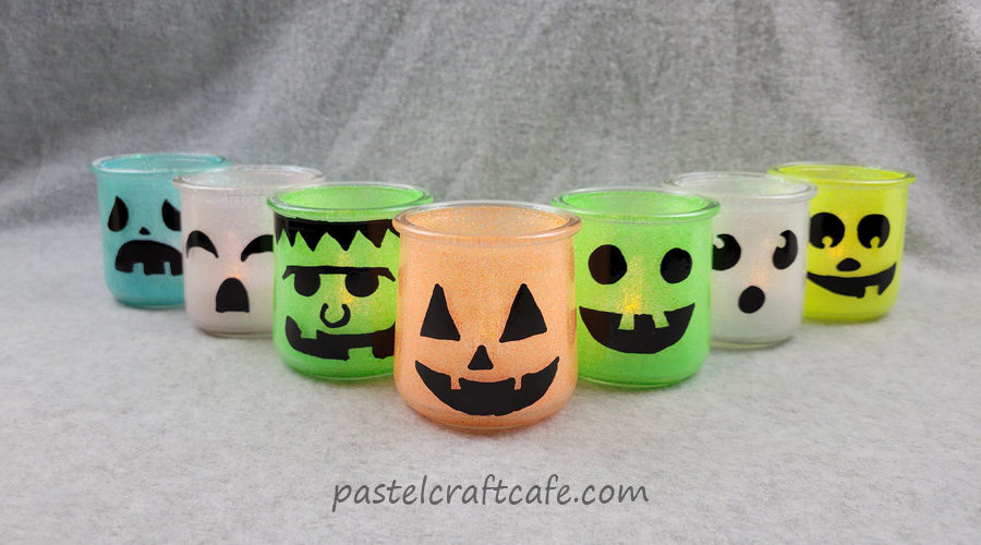 Seven glitter halloween luminary jars with various character faces in a V formation