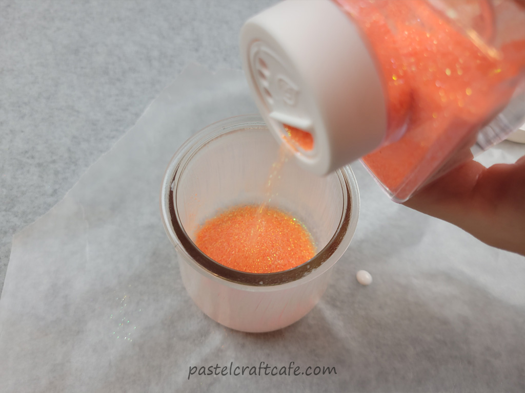 Orange glitter being poured into a glass jar