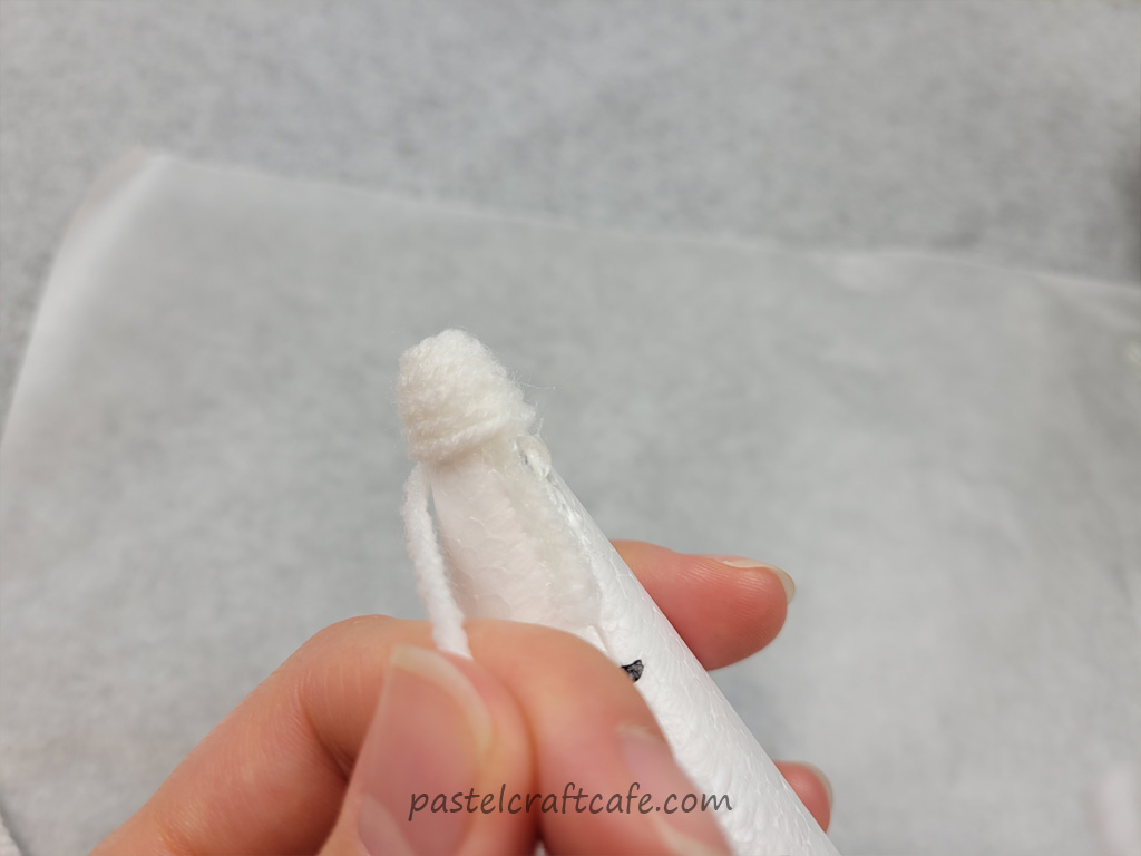 White yarn wrapped several times at the top of a styrofoam cone