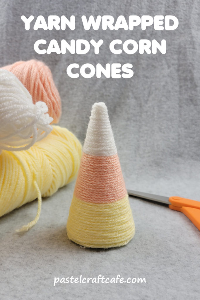 Text "Yarn Wrapped Candy Corn Cones DIY" above a cone wrapped in yarn to represent candy corn with skeins of colored yarn and a pair of scissors in the background