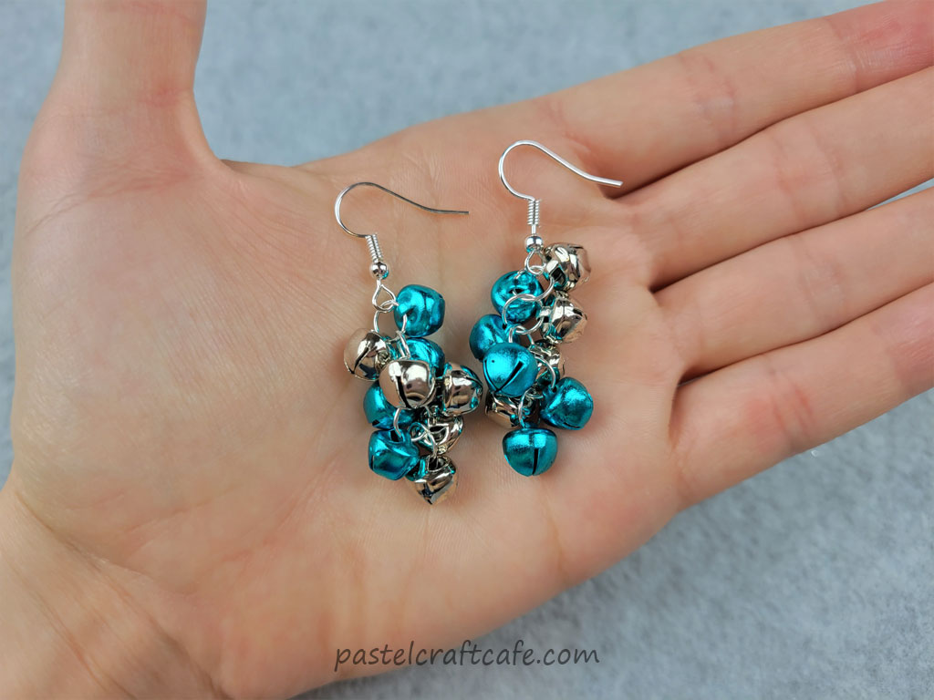 Two jingle bell cluster earrings sitting on a hand