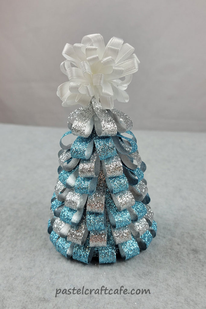 A ribbon christmas tree made of blue and silver ribbon with a white bow on top