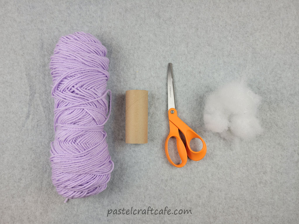 A skein of purple yarn, a toilet paper tube, scissors, and polyfill stuffing