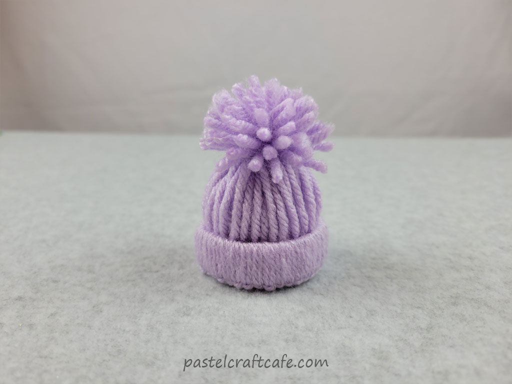 A finished mini yarn hat made with purple yarn