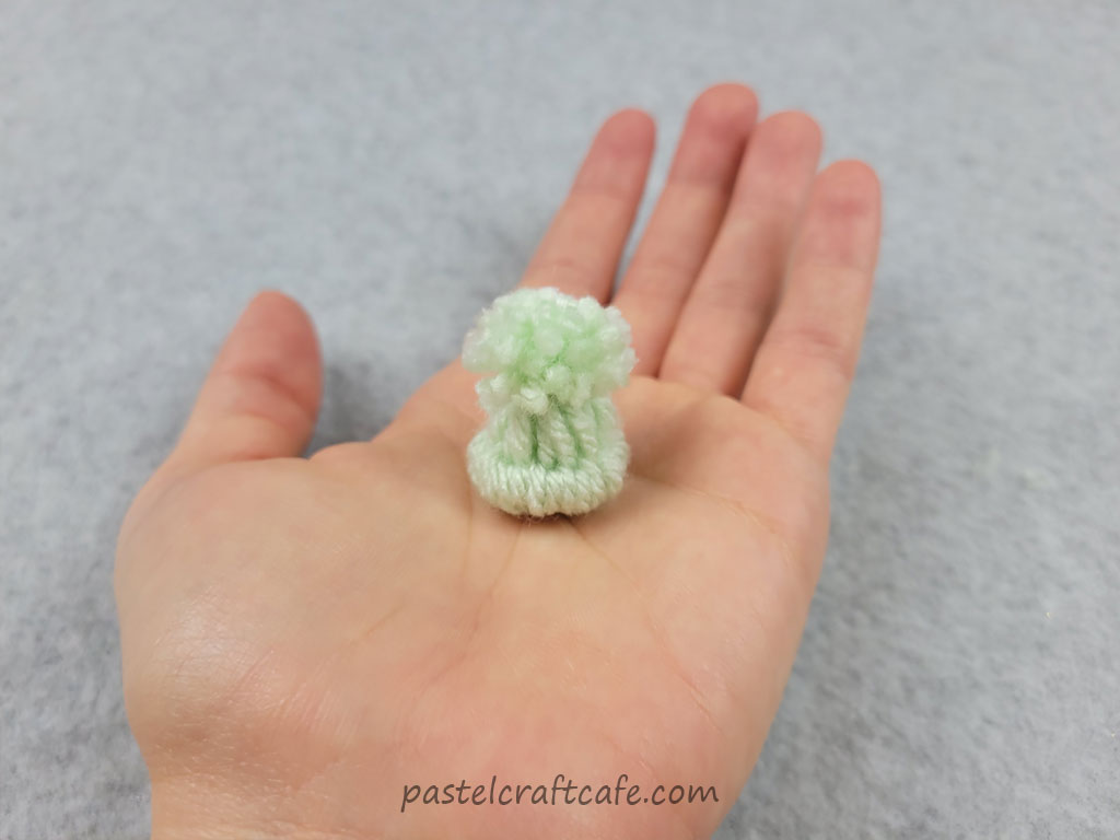 A very tiny mini yarn hat sitting on a hand