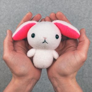 A small stuffed rabbit being held in the palms of two hands