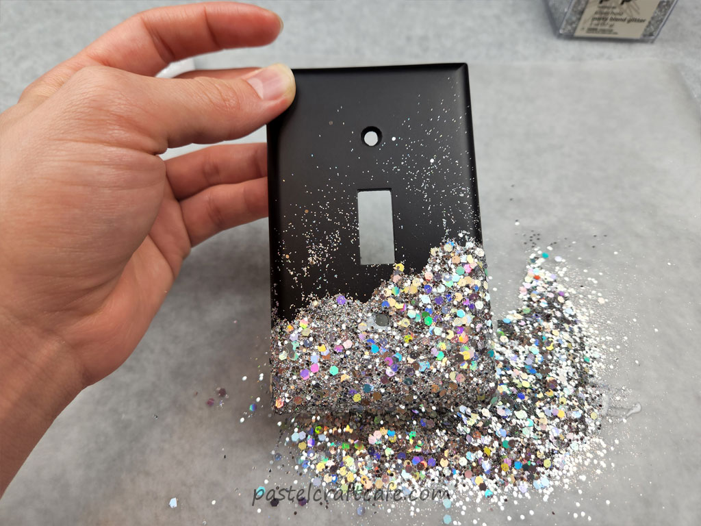 A messy layer of mixed holographic glitter covering the bottom end of a black lightswitch plate