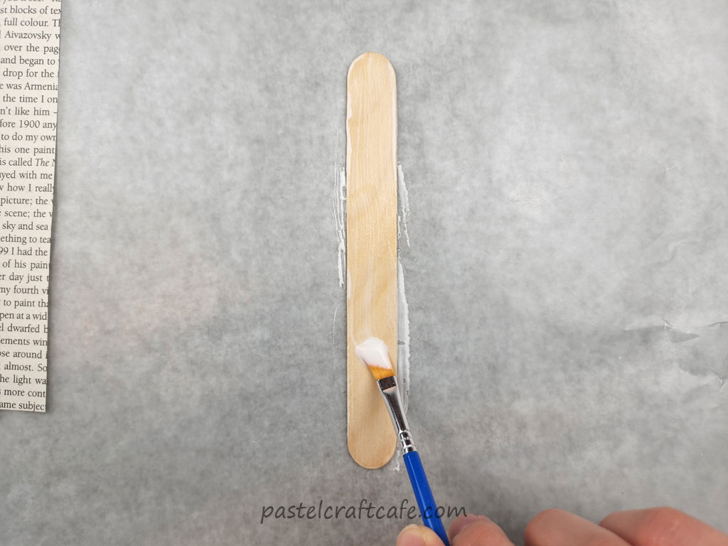 Mod Podge being brushed onto a popsicle stick using a paintbrush