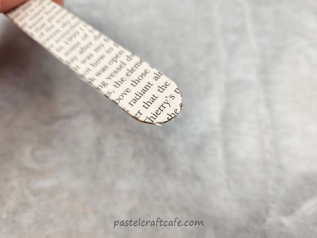 The unfinished edge of a paper popsicle stick bookmark. The paper edge is messy and rough.