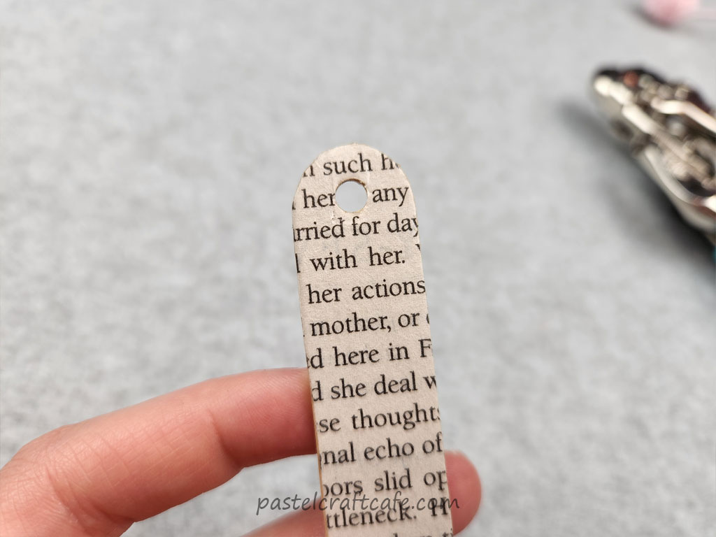 A hole punched at the top of a popsicle stick covered in book pages